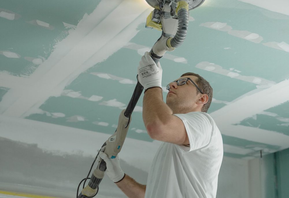Contractor sanding a newly installed ceiling board during a soundproofing upgrade
